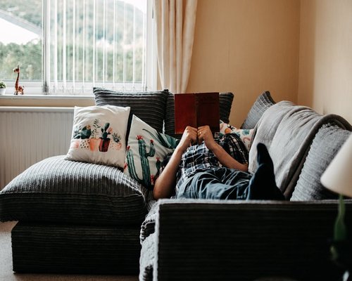 A person reading a book on a comfortable sofa with natural light coming from the window