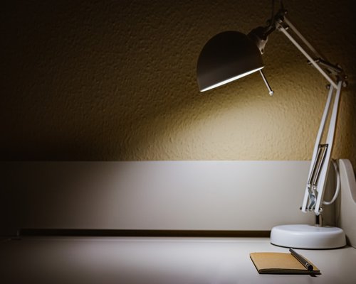 A warm desk lamp illuminating an open notebook on a wooden table