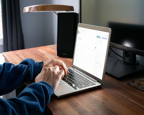 A person typing on a laptop with a smartphone resting on the desk